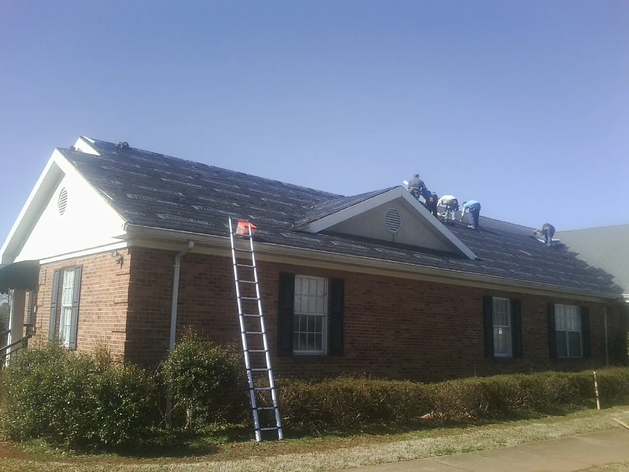 Crew tearing shingles off a brick ranch roof with a ladder set — Emergency Roof Repair work by our crew in Kimmswick