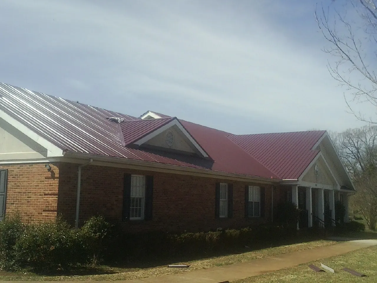 Red metal roof with gabled entries on a long brick building, from a Hail Damage Roof Repair job in Kimmswick