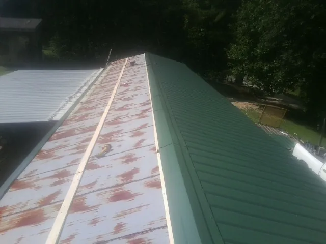Old rusted panels beside newly installed green metal roofing — Wind Damage Roof Repair by Roofing Brothers in Kimmswick