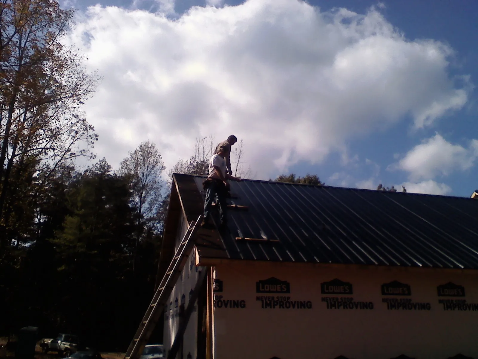 Roofer fastening dark metal panels high against a cloudy sky, from a Roof Inspection job in Kimmswick