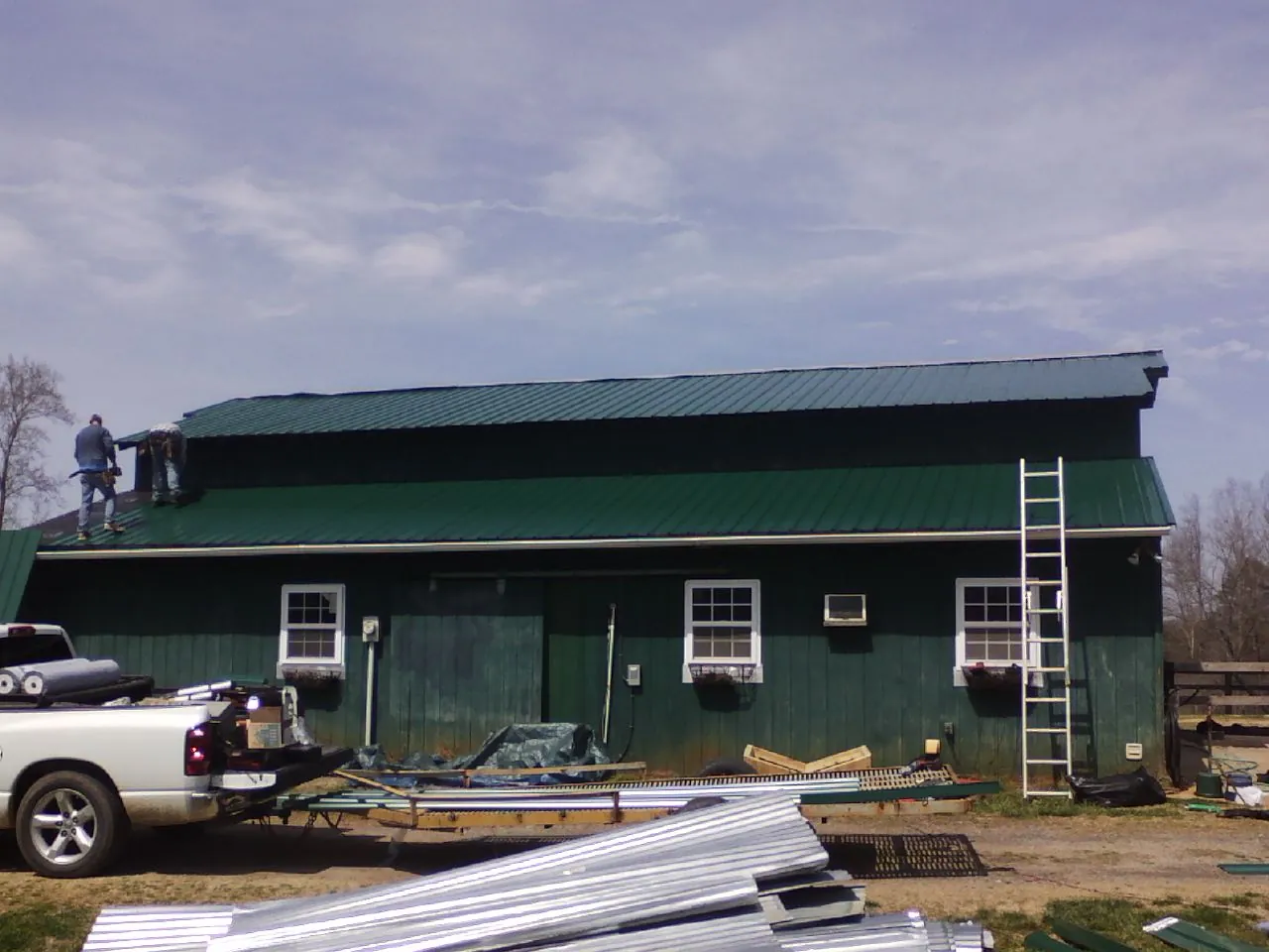 Crew installing green metal roofing on a large green barn in Kimmswick